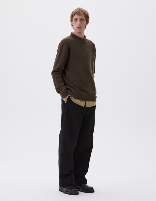 Full body image, front view of model wearing dark green oversized contrast rib crew neck jumper. Styled with dark yellow shirt over black pleated trousers with black leather boots.