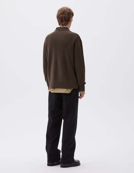 Full body image, back view of model wearing dark green oversized contrast rib crew neck jumper. Styled with dark yellow shirt over black pleated trousers with black leather boots.