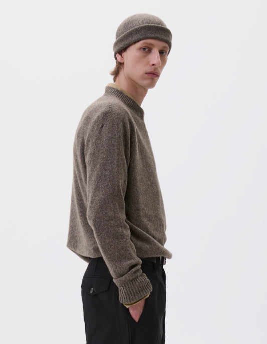 Cropped body image, side view of model wearing beige brown cashmere and wool beanie hat with rolled edge brim folded. Styled with matching jumper and black trousers.