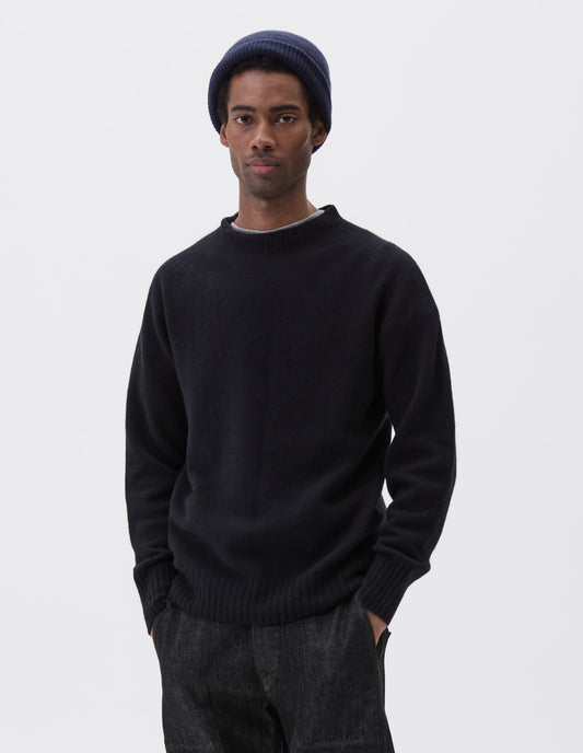 Cropped body image, front view of model wearing dark navy wool and cashmere jumper, with saddle sleeve, contrast rib on neck, cuffs and hem. Styled over grey t-shirt, with black denim jeans and navy blue beanie hat.