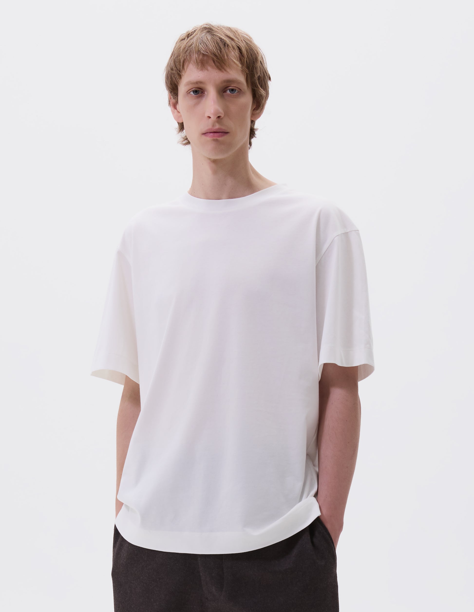 Cropped body image, front view of model wearing off white cotton short sleeve t-shirt. Styled with brown trousers.