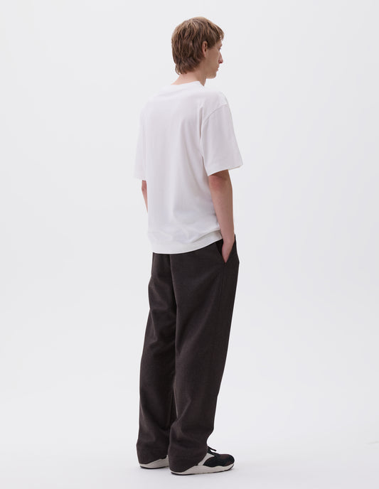 Full body image, back view of model wearing off white cotton short sleeve t-shirt. Styled with brown trousers and black and brown trainers.