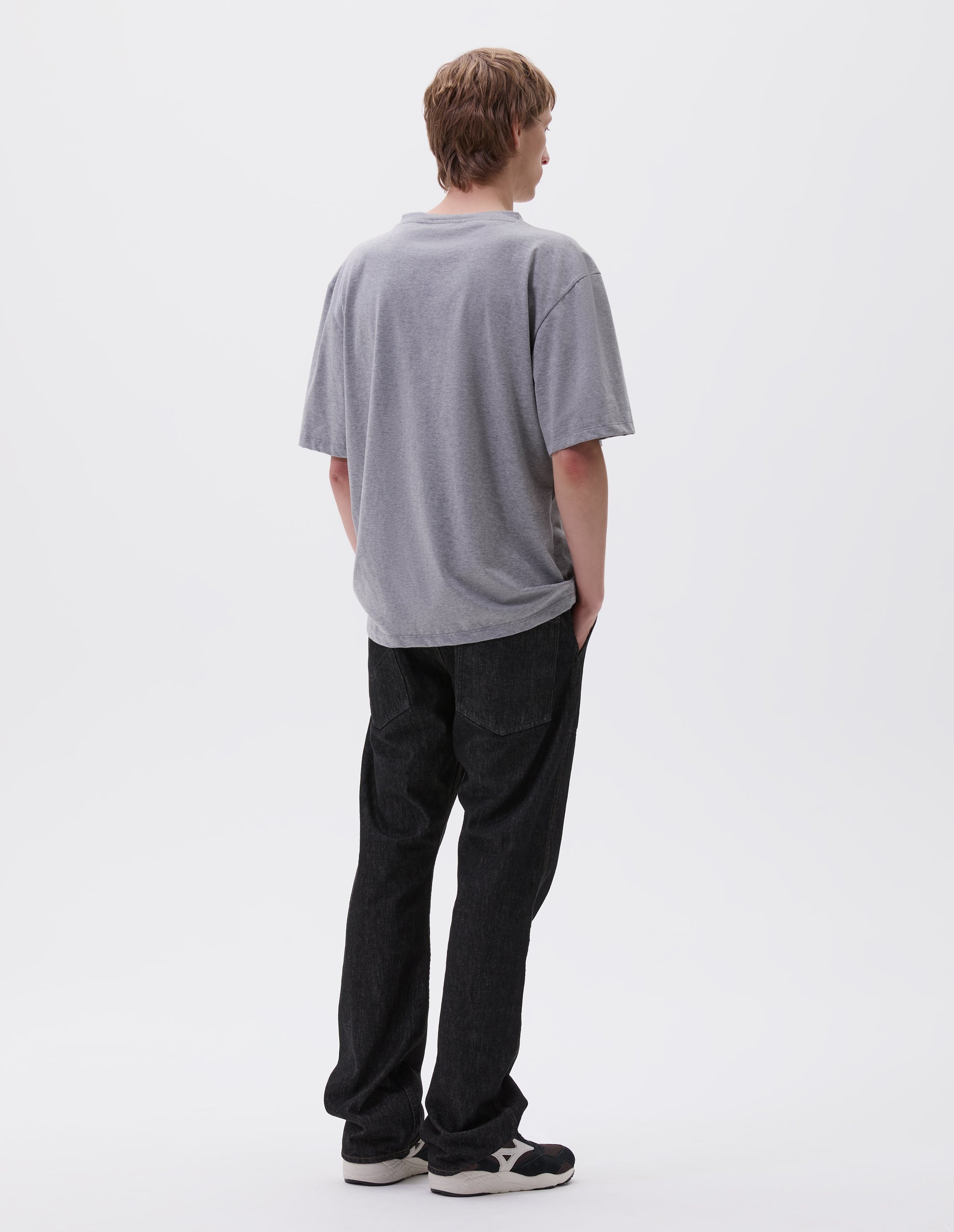 Full body image, back view of model wearing grey cotton short sleeve t-shirt.  Styled with black denim jeans and black and brown trainers.