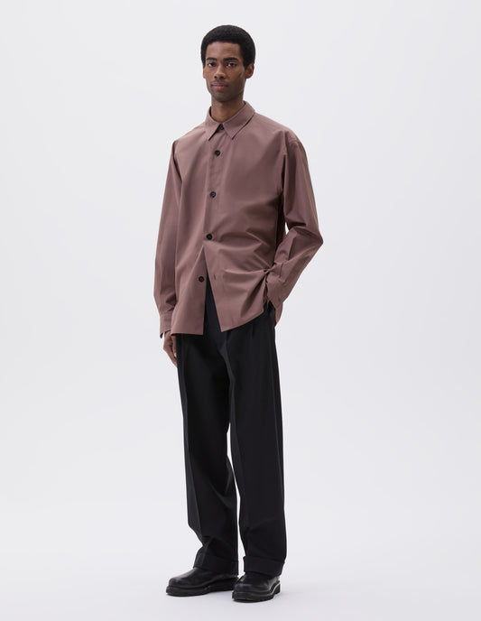 Full body image, front view of model wearing relaxed dark pink shirt with stitch through placket and mother of pearl buttons. Styled with black trousers and black leather boots.