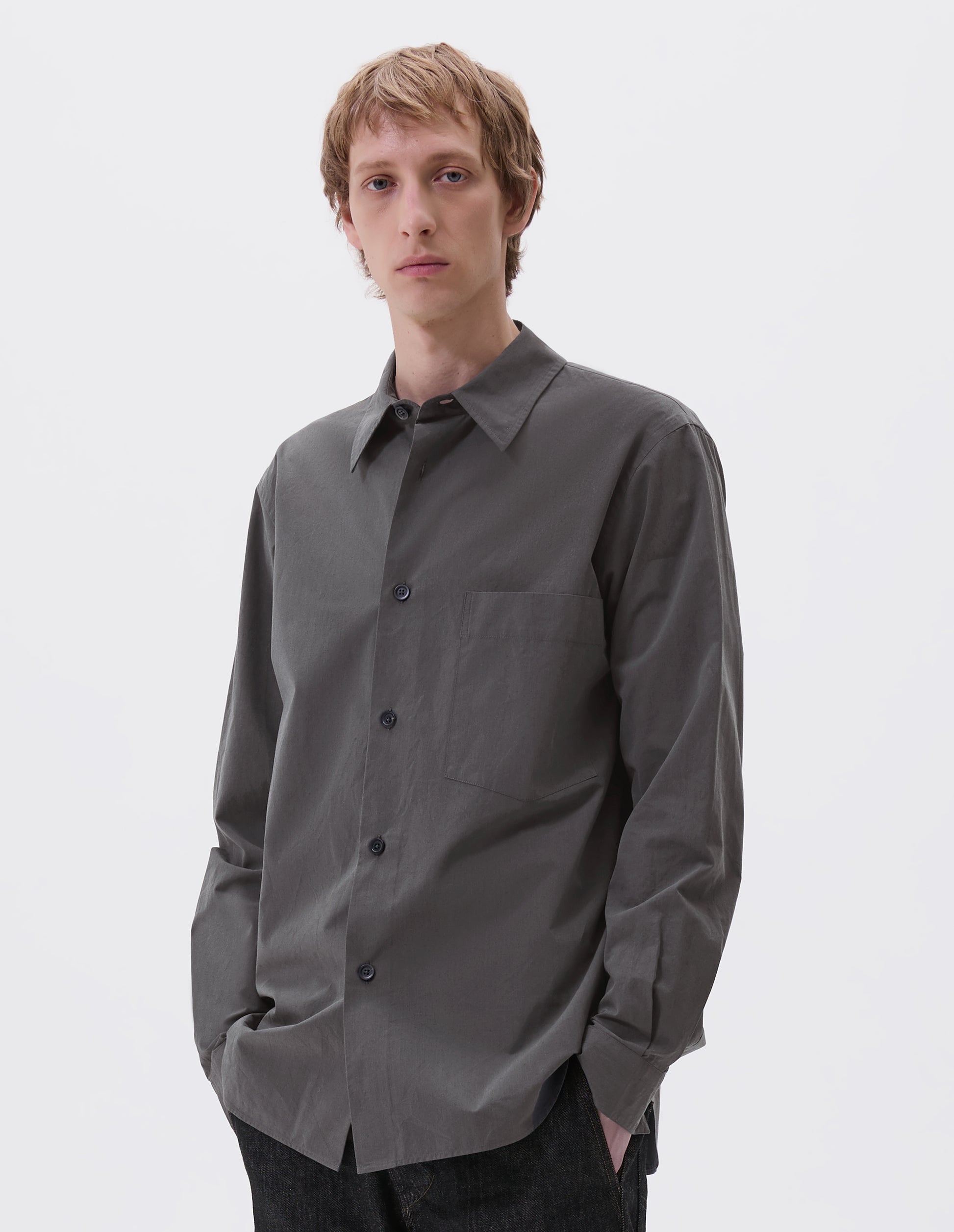Cropped image, front view of model wearing regular cut dark grey shirt with chest pocket and horn buttons. Styled with black jeans.