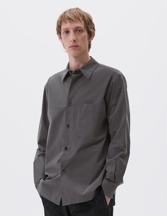 Cropped image, front view of model wearing regular cut dark grey shirt with chest pocket and horn buttons. Styled with black jeans.