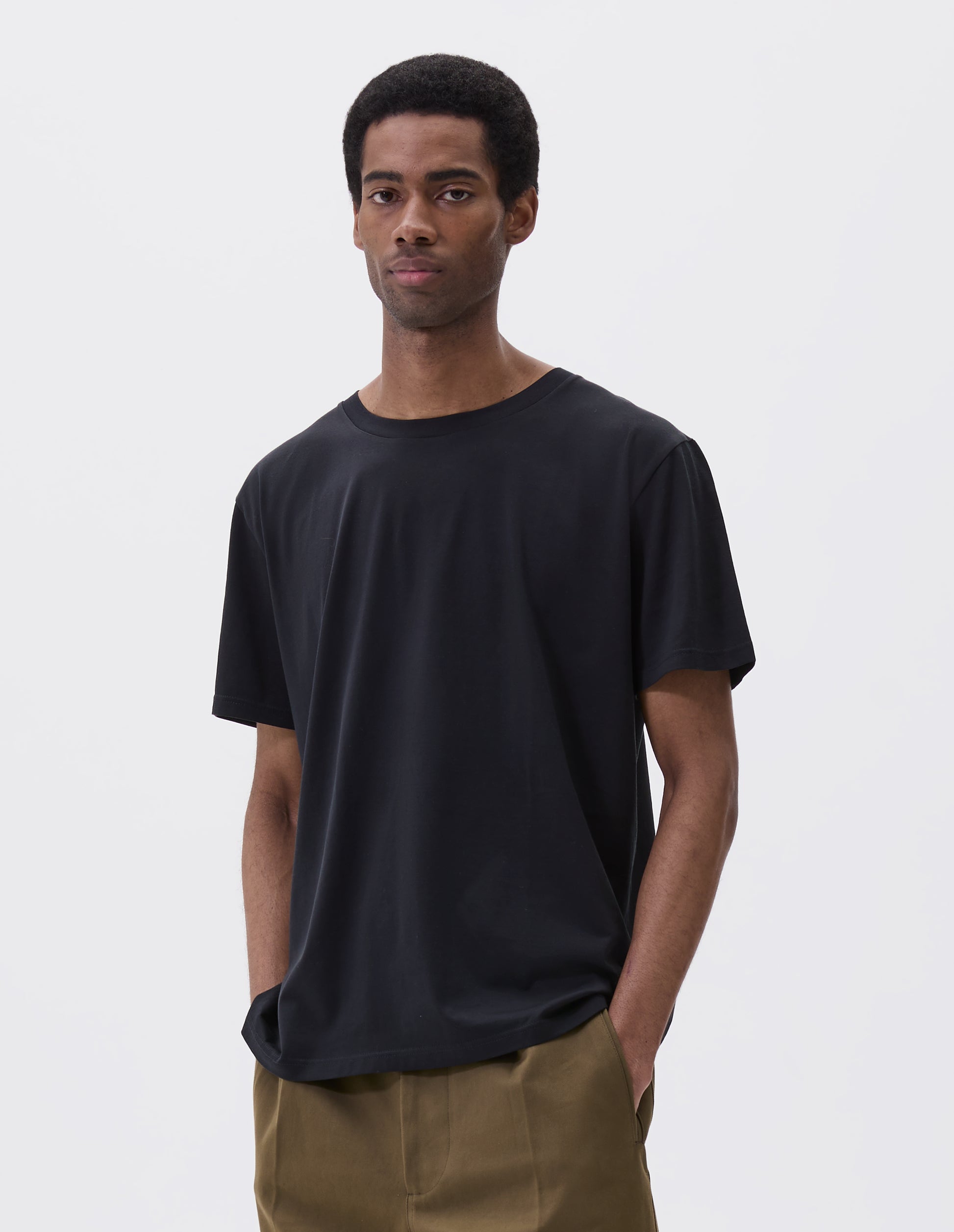 Cropped body image, front view of model wearing black cotton short sleeve t-shirt. Styled with green trousers.