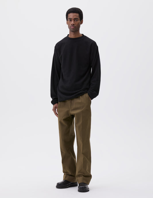 Full body image, front view of model wearing relaxed black crew neck jumper with rolled edge detailing on neck, rib trim on cuffs and hem. Styled with khaki green trousers and black leather boots.