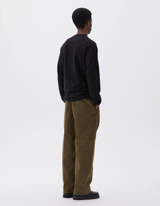 Full body image, back view of model wearing relaxed black crew neck jumper with rolled edge detailing on neck, rib trim on cuffs and hem. Styled with khaki green trousers and black leather boots.