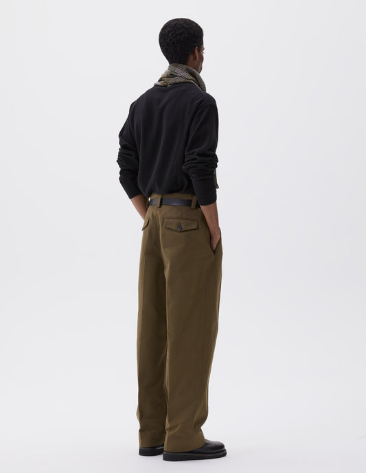 Full body image, back view of model wearing brown green heavy cotton trousers, with belt loops and concealed and button-through jet back pockets. Styled with black jumper, green, white and brown checked scarf black leather belt and black leather boot.