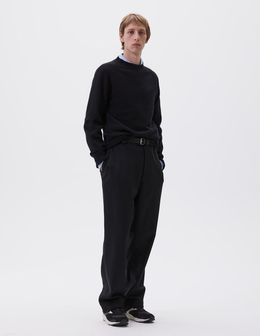 Full body image, front view of model wearing navy blue trousers, with half elasticated waistband, belt loops, horn button tab fastening and slant pockets. Styled with blue shirt, navy jumper, black leather belt and black and brown trainers.