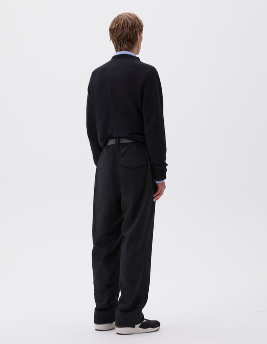 Full body image, back view of model wearing navy blue trousers, with half elasticated waistband, belt loops and welt and concealed button fastening flap back pockets. Styled with blue shirt, navy jumper, black leather belt and black and brown trainers.