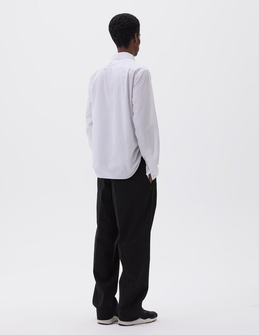 Full body image, back view of model wearing regular cut white shirt with grey stripes, curved hem, pleats on back yoke and mother of pearl buttons on cuffs. Styled with black trousers and black, brown and white trainers.