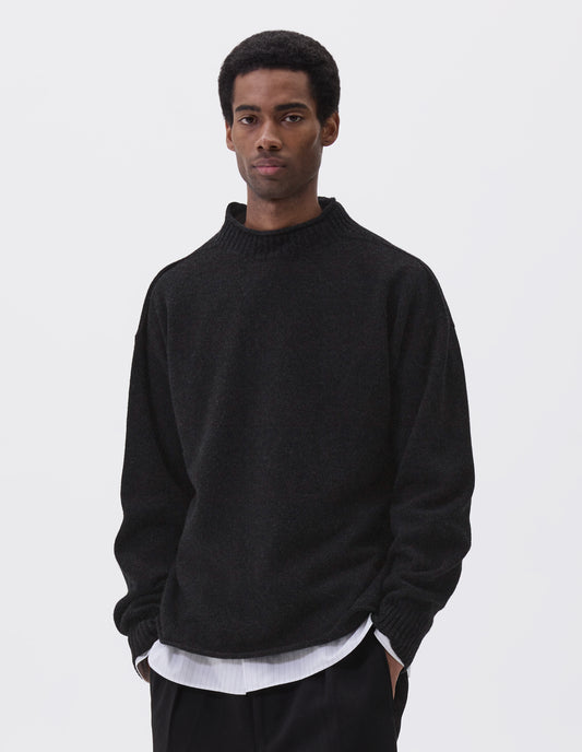 Cropped body image, front view of model wearing black long sleeve jumper with rolled edge neck and hem and contrasting rib on neck and sleeves. Styled with black trousers and white and grey striped shirt.