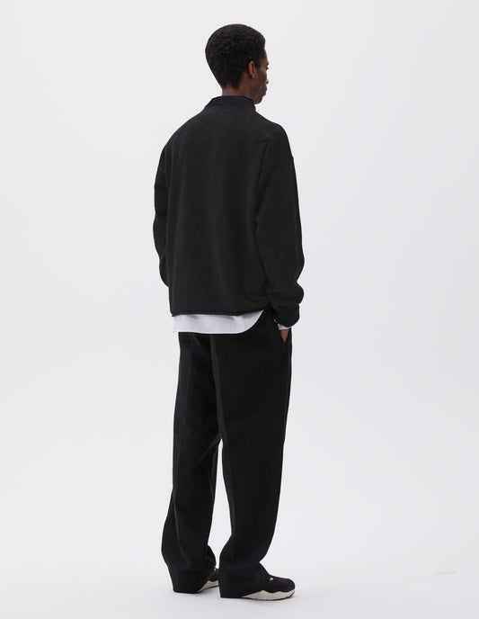 Full body image, back view of model wearing black long sleeve jumper with rolled edge neck and hem and contrasting rib on neck and sleeves. Styled with black trousers, white and grey striped shirt and black and brown trainers.