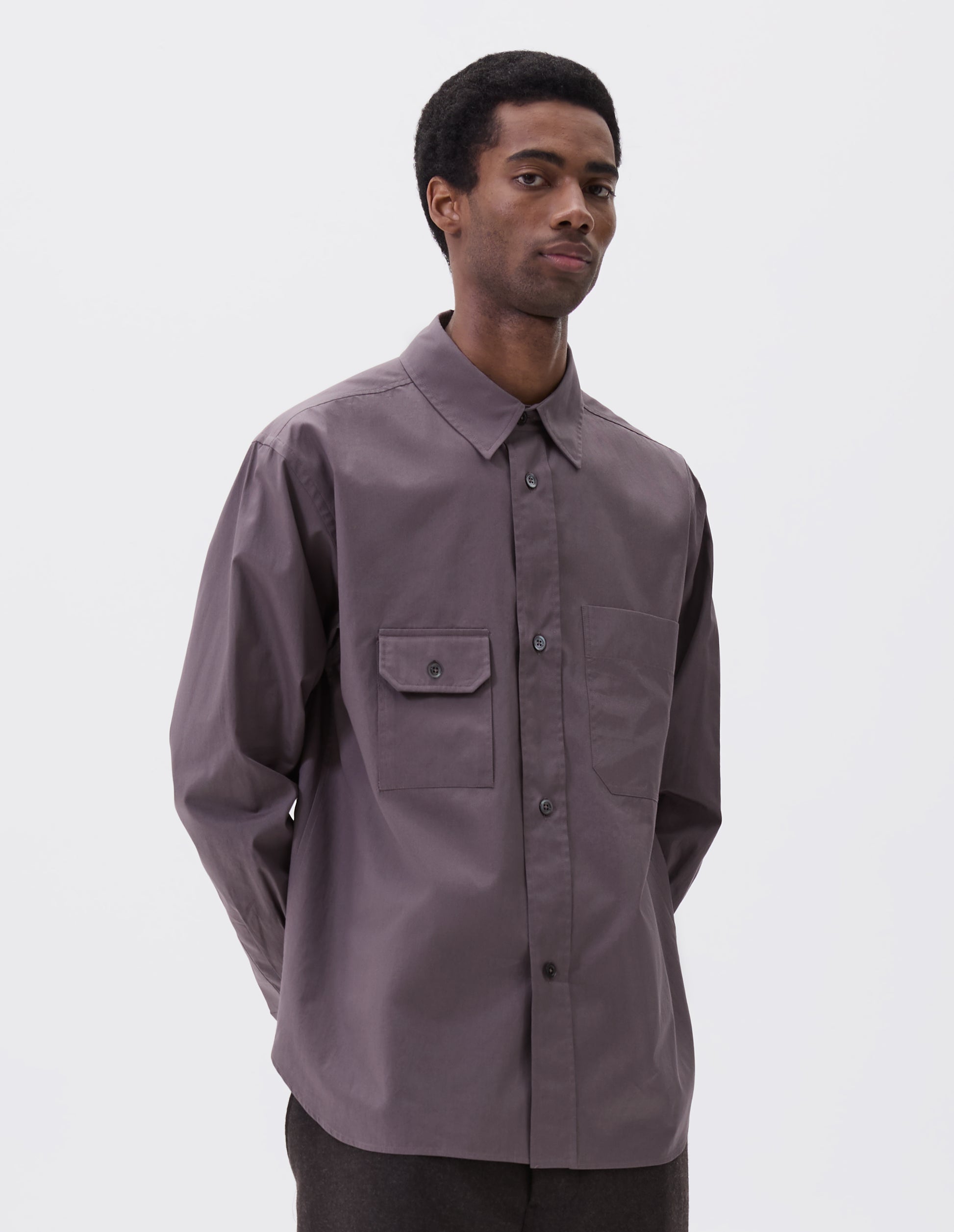 Cropped image, front view of model wearing grey shirt with patch pocket and button-through flap pocket on chest, raised placket with mother of pearl buttons, styled with dark grey trousers.