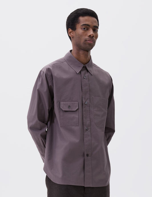 Cropped image, front view of model wearing grey shirt with patch pocket and button-through flap pocket on chest, raised placket with mother of pearl buttons, styled with dark grey trousers.