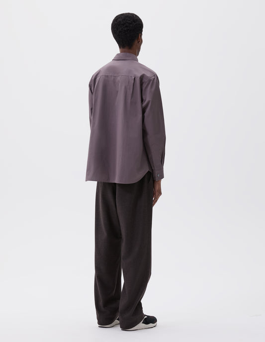 Full body image, back view of model wearing grey shirt with mother of pearl buttons on cuffs, styled with dark grey trousers and black, brown and white trainers.