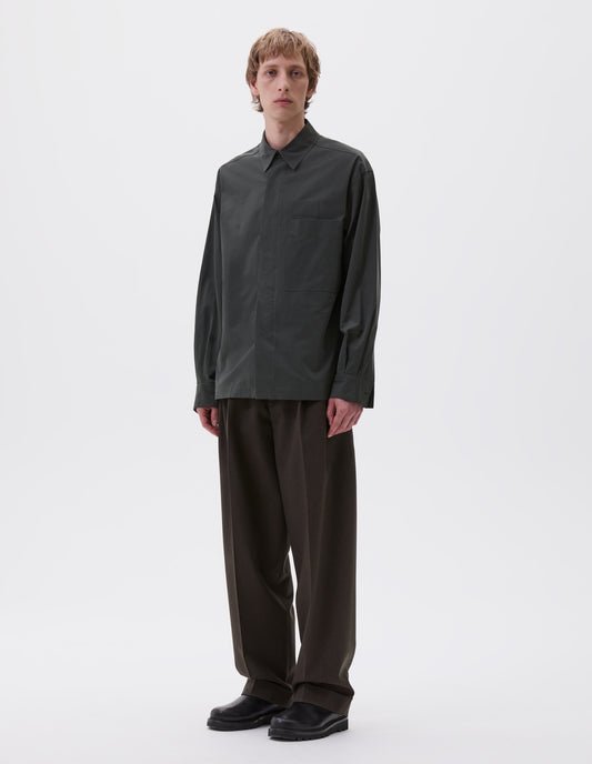 Full body image, front view of model wearing dark green shirt with wide placket, large patch chest pocket with internal pen pocket, styled with dark brown trousers and black leather shoes.