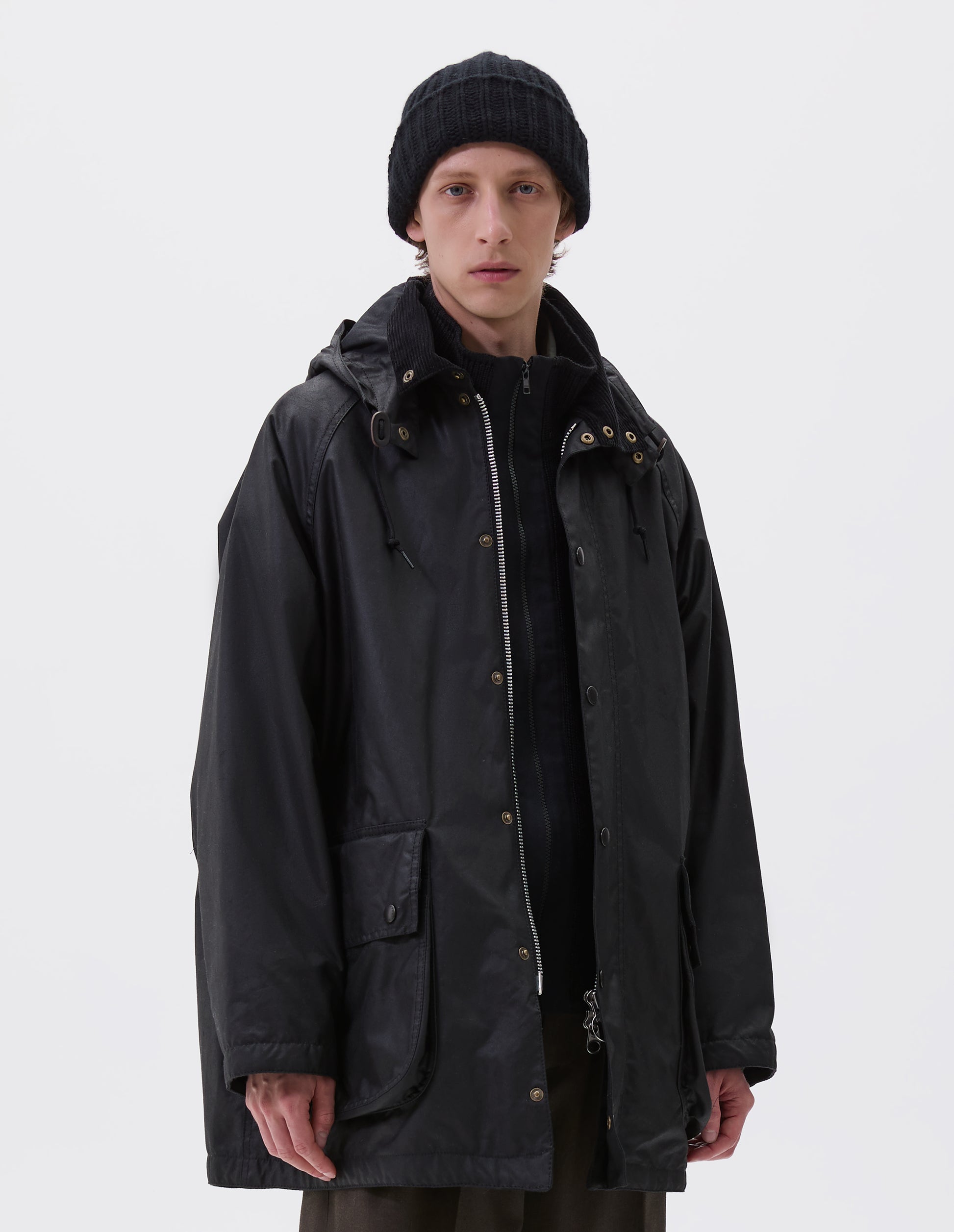 Cropped body image, front view of male model wearing black chunky knitted cashmere beanie, styled with black waxed jacket, black zip up knitted cardigan and beige trousers.