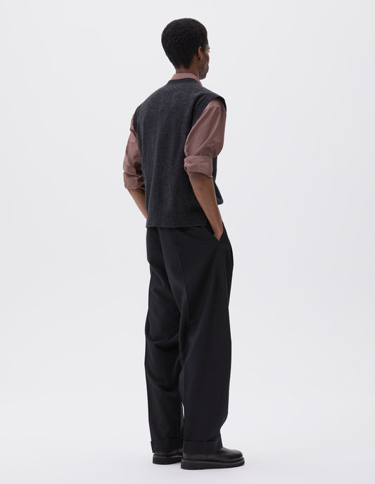 Full body image, back view of model wearing Charcoal grey sleeveless knitted jumper, with contrast rib on neck, armholes and hem. Styled with pink shirt, black trousers and black leather boots.