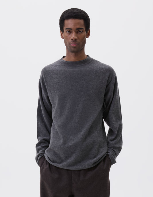 Cropped image, front view of model wearing relaxed grey crew neck jumper with rolled edge detailing on neck, rib trim on cuffs and hem. Styled with brown trousers.