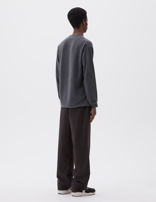 Full body image, back view of model wearing relaxed grey crew neck jumper with rolled edge detailing on neck, rib trim on cuffs and hem. Styled with brown trousers and black, brown and white trainers.