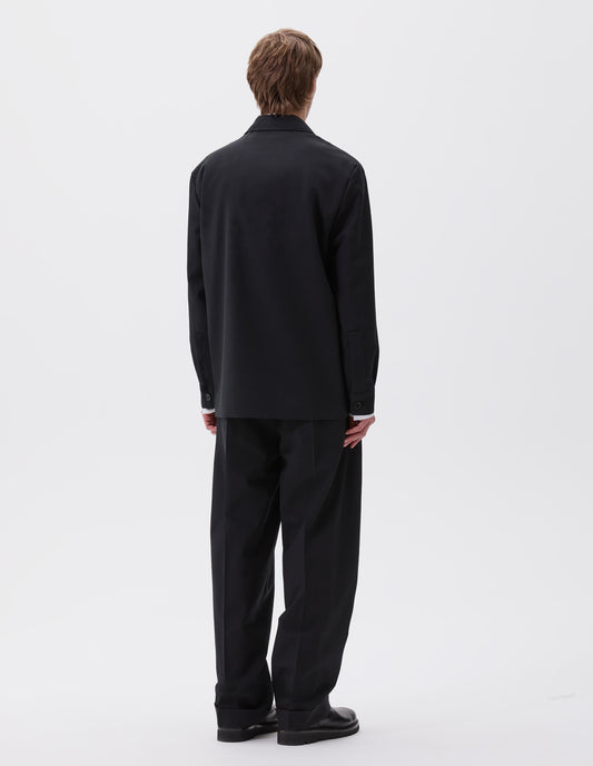 Full body image, back view of model wearing black wool blazer with horn button shirt cuffs. Styled with matching black trousers and black leather boots.