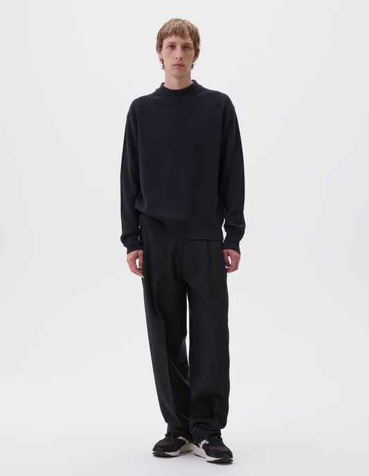Full body image, front view of model wearing dark blue oversized contrast rib crew neck jumper. Styled with black  pleated trousers and black, brown and white trainers.