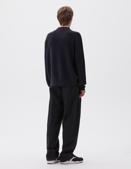 Full body image, back view of model wearing dark blue oversized contrast rib crew neck jumper. Styled with black  pleated trousers and black, brown and white trainers.