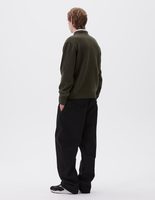 Full body image, back view of model wearing dark green ribbed crew neck jumper with ribbed cuffs and hem, styled over white striped shirt, black trousers and black, brown and white trainers.