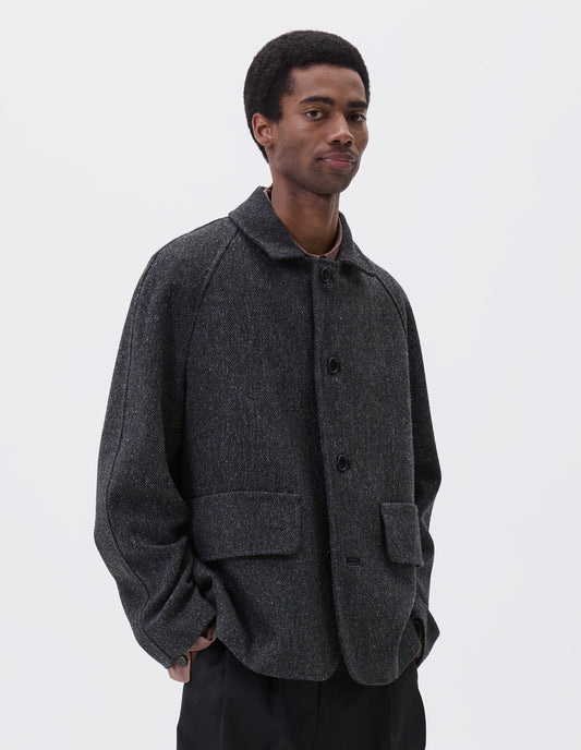 Cropped body image, front view of model wearing grey wool blazer with high collar fastening, deep flap welt pockets and subtle horn button detailing. Styled over pink shirt, with black trousers.