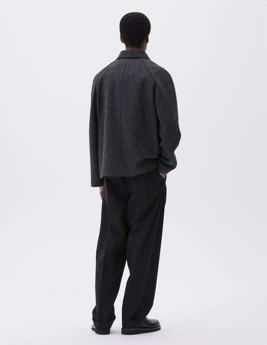 Full body image, back view of model wearing grey wool blazer with high collar fastening and raglan sleeve Styled with black trousers and black leather boots. 