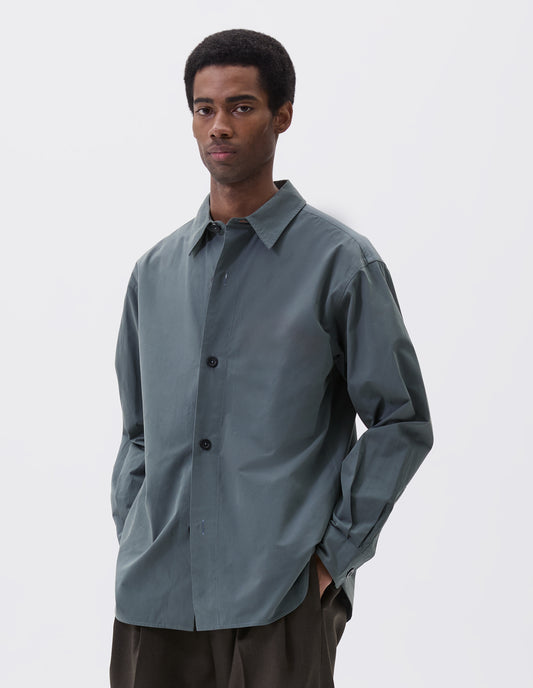 Cropped image, front view of model wearing relaxed blue shirt with stitch through placket and horn buttons. Styled with khaki green trousers.