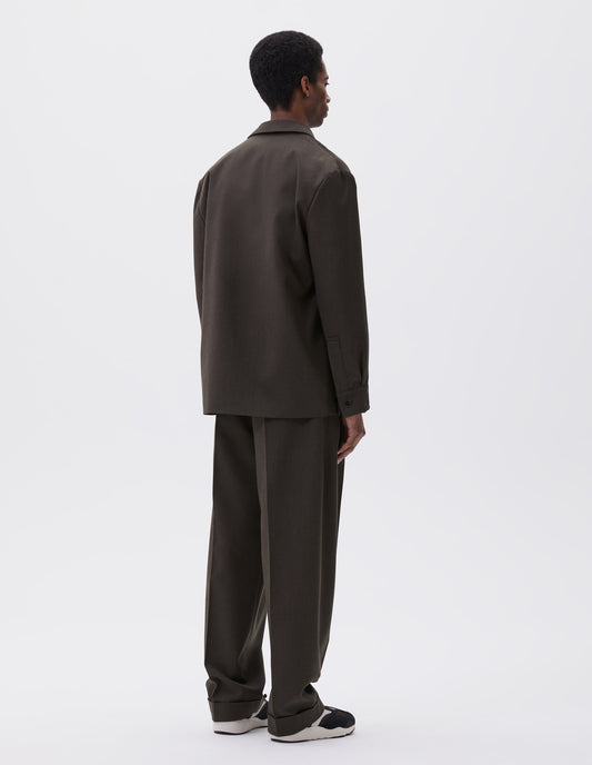 Full body image, back view of model wearing brownish green wool blazer with horn button shirt cuffs. Styled with matching brownish green trousers and black and brown trainers.