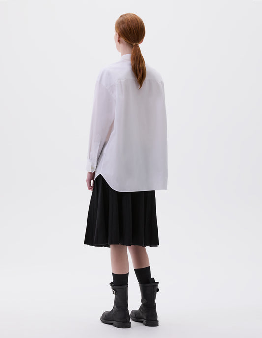 Full body image, back view of model wearing relaxed white shirt with mother of pearl buttons on turned up cuffs. Styled with black skirt, black socks and black leather biker boots.