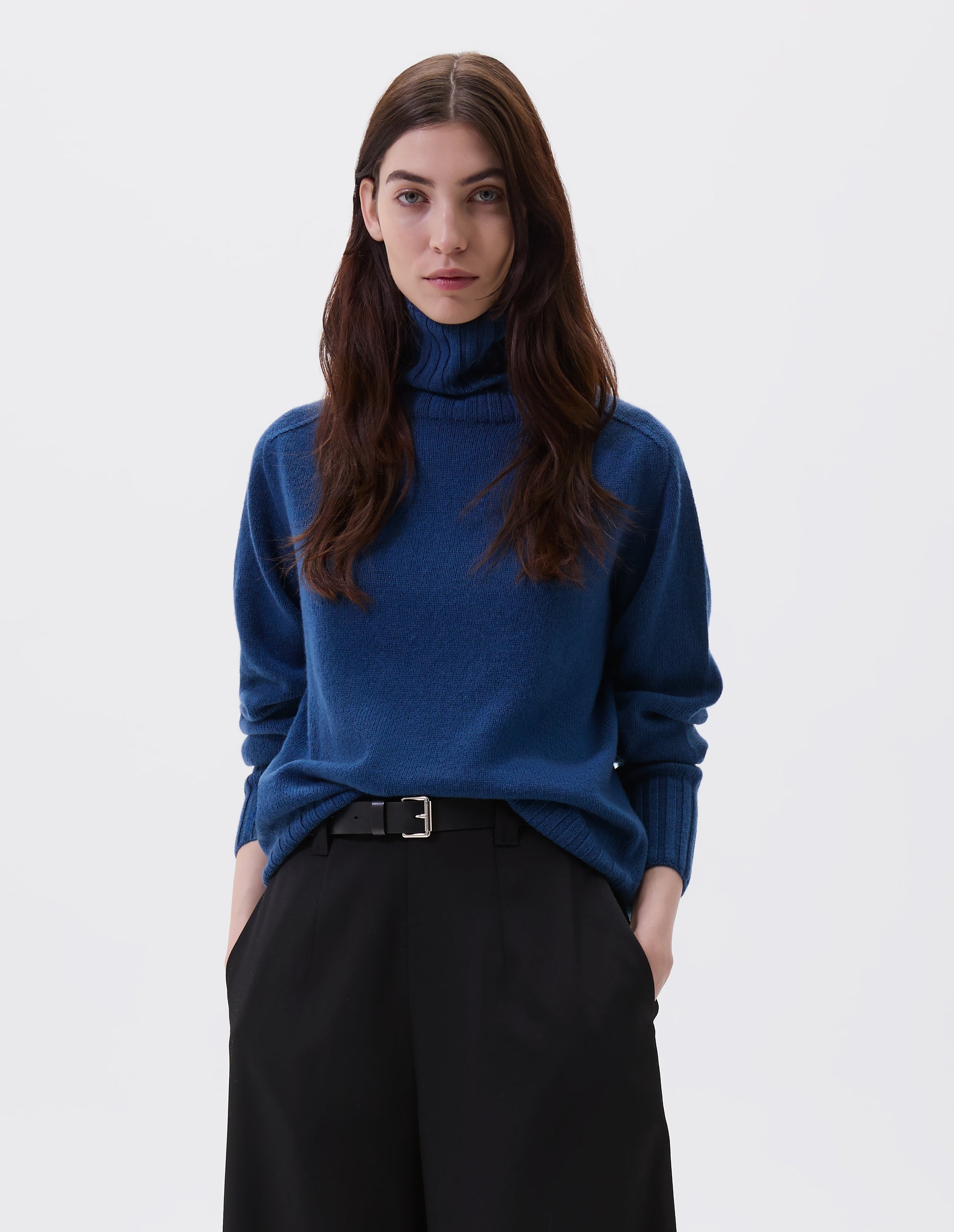 Cropped body image, front view of female model wearing black leather belt with silver buckle and black leather strap. Styled with blue high neck jumper and black wool culottes.