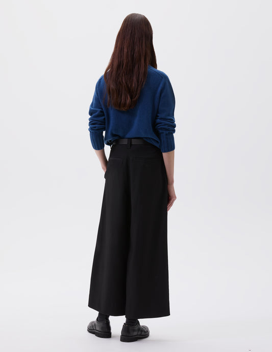 Full body image, back view of model wearing black wool wide leg culottes, with belt loops, side pockets and welt back pockets. Styled with blue turtleneck jumper, black leather belt and black leather brogues.