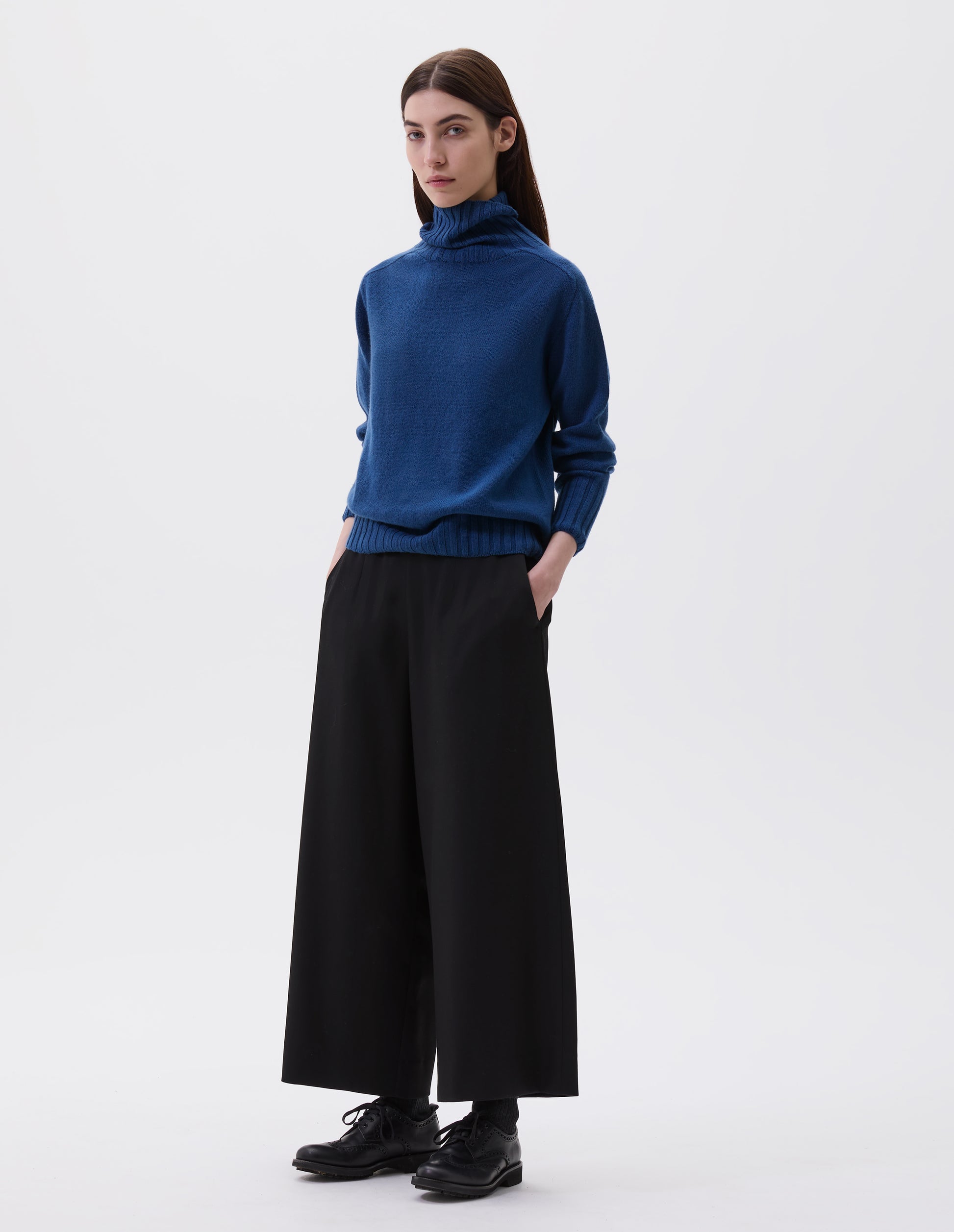 Full body image, front view of model wearing a pair of matt black leather brogues with black laces and lightweight rubber commando sole. Styled with blue high neck jumper and black culottes. 
