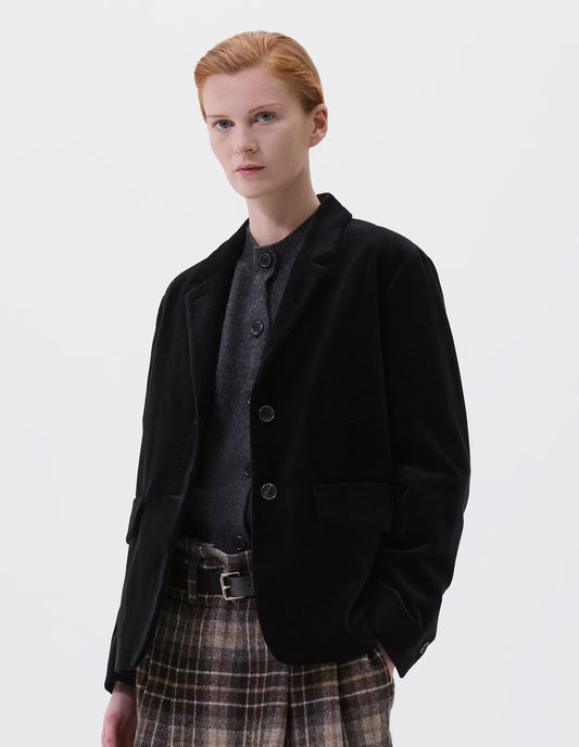 Cropped body image, front view of model wearing black blazer with horn buttons on lapel and cuffs.  Styled over dark grey slipover and with brown tartan skirt and black leather belt.