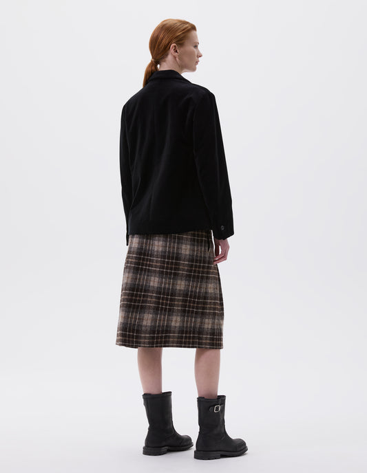 Full body image, back view of model wearing black blazer with horn buttons on cuffs. Styled with brown tartan skirt and black leather biker boots.