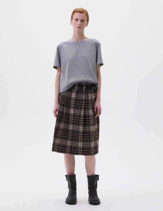 Full body image, front view of model wearing grey cotton short sleeve t-shirt with boxy cut. Styled with brown and beige check skirt, black leather belt and black leather boots.