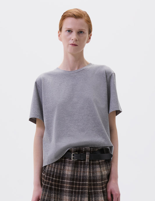 Cropped body image, front view of model wearing grey cotton short sleeve t-shirt with boxy cut. Styled with brown and beige check skirt and black leather belt.