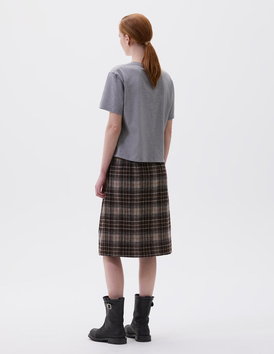 Full body image, back view of model wearing grey cotton short sleeve t-shirt with boxy cut. Styled with brown and beige check skirt and black leather boots.