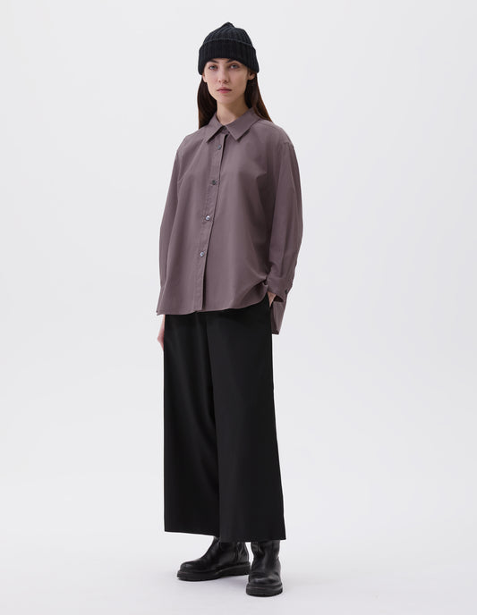 Full body image, front view of model wearing relaxed brown shirt with raised, stitch-through placket with mother of pearl buttons and A line hem. Styled with black beanie, black culottes and black leather boots.