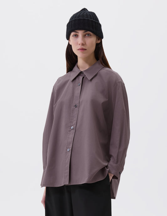 Cropped image, front view of model wearing relaxed brown shirt with raised, stitch-through placket with mother of pearl buttons and A line hem. Styled with black beanie and black culottes.