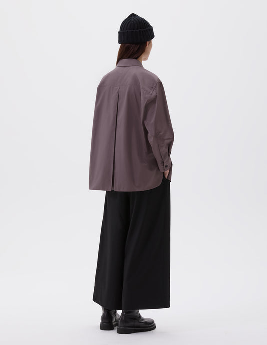Full body image, back view of model wearing relaxed brown shirt with A line hem, split panel yoke with deep, inverted centre back pleat and mother of pearl buttons on cuffs. Styled with black beanie, black culottes and black leather boots.