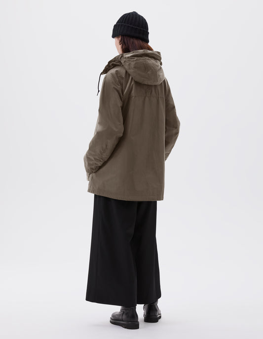 Full body image, back view of model wearing oversized dark beige parka with adjustable hood and raglan sleeves. Styled with black beanie, black culottes and black leather boots.