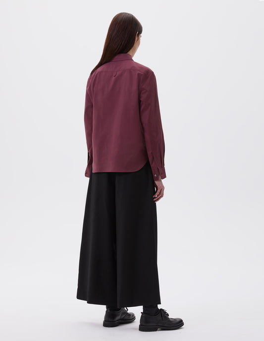 Full body image, back view of model wearing dark red shirt with mother of pearl buttons on cuffs, styled with black trousers and black socks with  brogues.