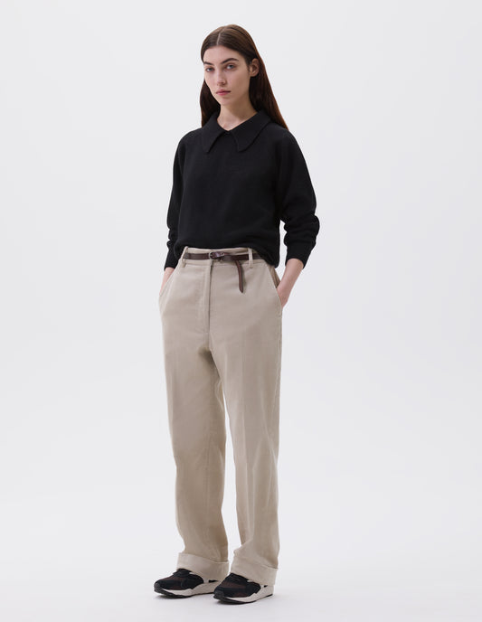 Full body image, front view of model wearing beige corduroy long leg trousers, with belt loops and side pockets. Styled with black jumper, brown leather belt and black and brown trainers.